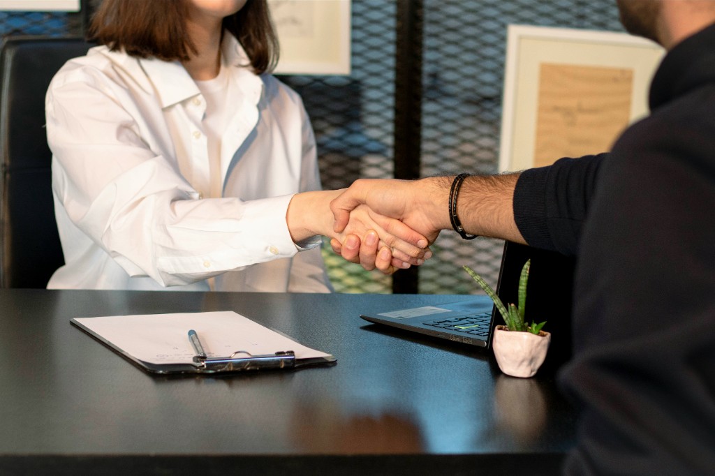 Two professionals shaking hands across a desk after a successful meeting or interview